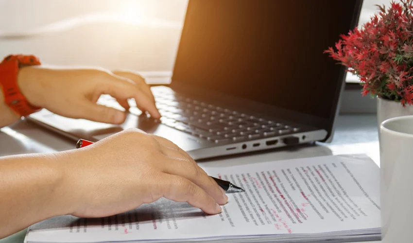 Person writing on paper while using a laptop.